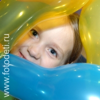 Ребёнок с счастливыми глазами выглядывает из связки надувных шариков, выступления клоунов перед детьми
