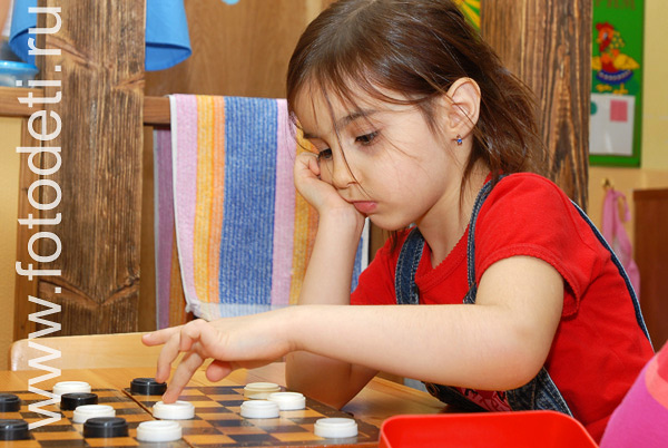 Физическое развитие детей. Девочка обдумывает ход, играя в шашки.