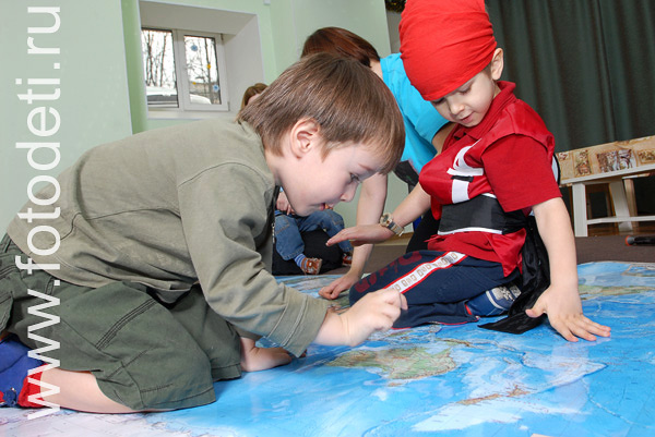 На фото дети учатся. Дети играют на географической карте.