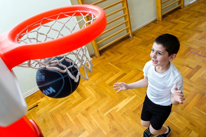 Ребенок забрасывает мяч в баскетбольное кольцо на физкультуре в детском саду