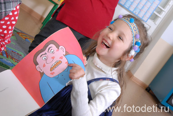 Фотографии детей. Девочка смеётся над картинкой из книги для детей.