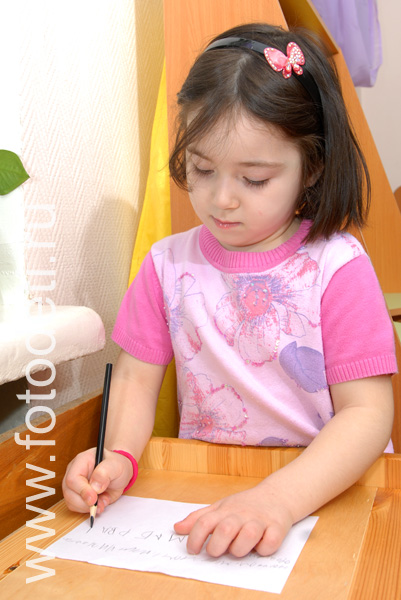 На фото дети в процессе обучения: Девочка пишет карандашом.