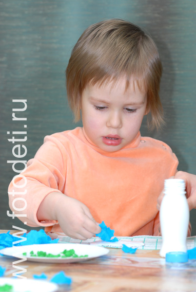 Дети на фото детского фотографа: Девочка наклеивает обрывки цветной бумаги на картонную тарелочку.