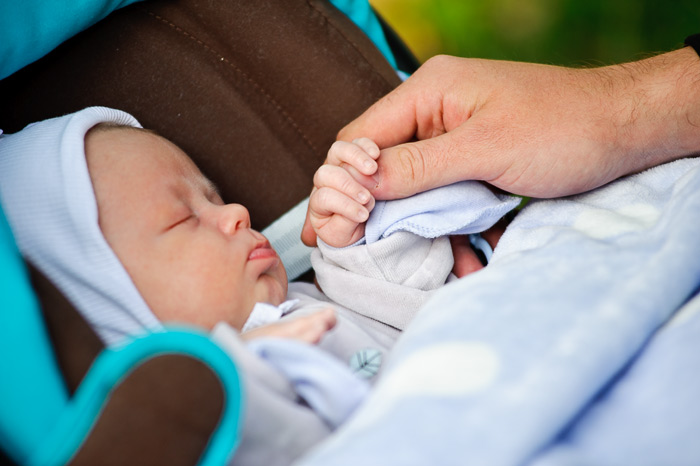 Фотосъёмка новорождённых детей. Младенец держится за папину руку.