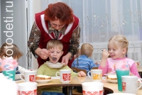 Воспитатель кормит ребёнка с ложечки, дети кушают самостоятельно