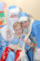 Ребёнок на коленях у Деда Мороза держит Снегурочку за косу, новогодние фотосессии