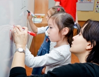Учитель помогает ребёнку писать маркером на доске. Фото детей на фотосайте Игоря Губарева.