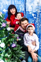 Семейное фото на фоне новогодних атрибутов - ёлочки и органзы с серебряными снежинками. Фото детей на фотосайте Игоря Губарева.