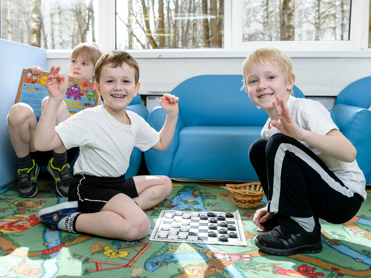 Дети играют в шашки на фотосессии один день в детском саду. Детский фотограф ирина Левитэ.